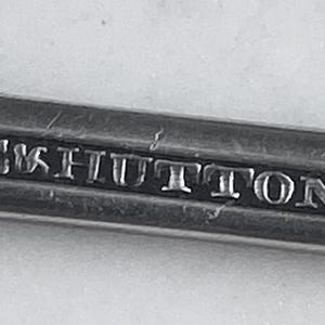 May include: Close-up of a silver metal object with the inscription "E & S Hutton" engraved on it.