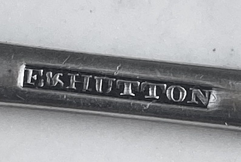 May include: Close-up of a silver metal object with the inscription "E & S Hutton" engraved on it.
