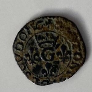 May include: A silver coin with a crown and a letter G in the centre. The coin is surrounded by a circular inscription.