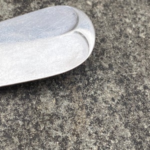 May include: Close-up of the rounded end of a silver spoon with a textured surface.