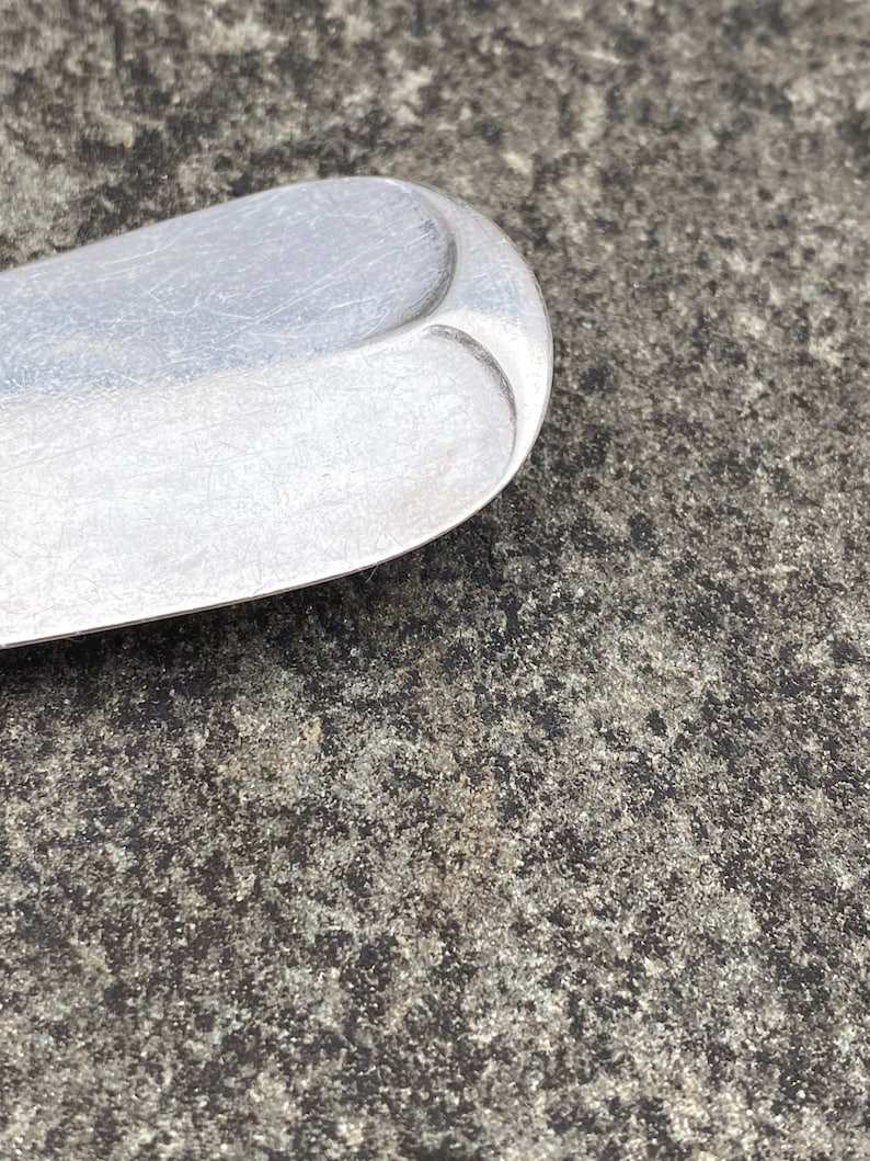 May include: Close-up of the rounded end of a silver spoon with a textured surface.