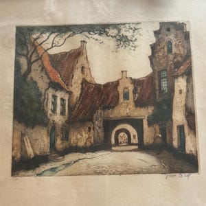 May include: An antique print of a European village scene. The artwork depicts buildings with red-tiled roofs, arched doorways, and cobblestone streets. The color palette is muted, with shades of brown, beige, and touches of green from the foliage.