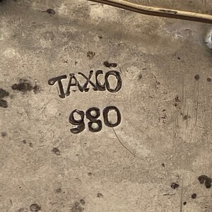 May include: Close-up of a silver pin with the words "Taxco 980" stamped on the back.