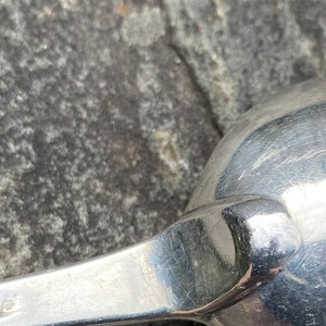 May include: Close-up of a silver spoon with a rounded bowl and a long, slender handle. The spoon is lying on a rough, gray surface.