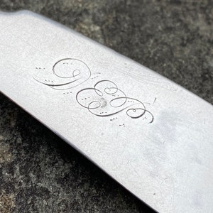 May include: Close-up of a silver shoe horn with an engraved monogram. The monogram is a stylized "W" with a flourish.