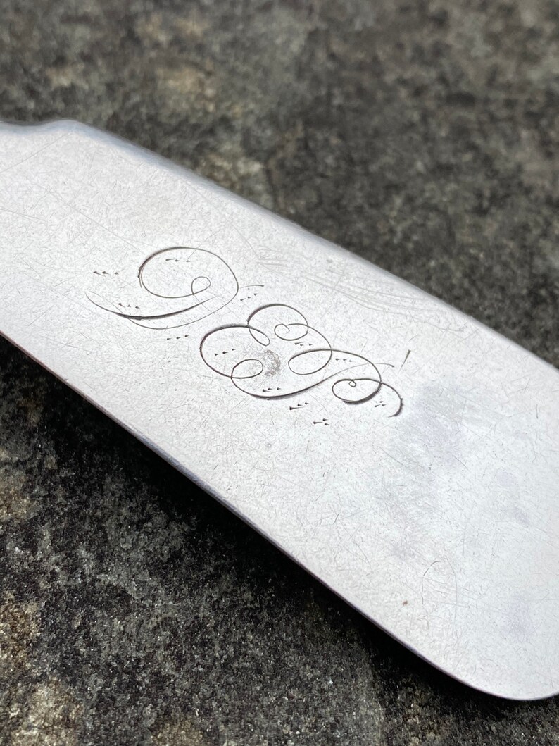 May include: Close-up of a silver shoe horn with an engraved monogram. The monogram is a stylized "W" with a flourish.