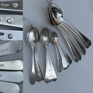 May include: A set of eight silver teaspoons with ornate handles. The spoons are arranged in a fan shape, with the largest spoon at the top and the smallest spoon at the bottom. The spoons are all polished and shiny.