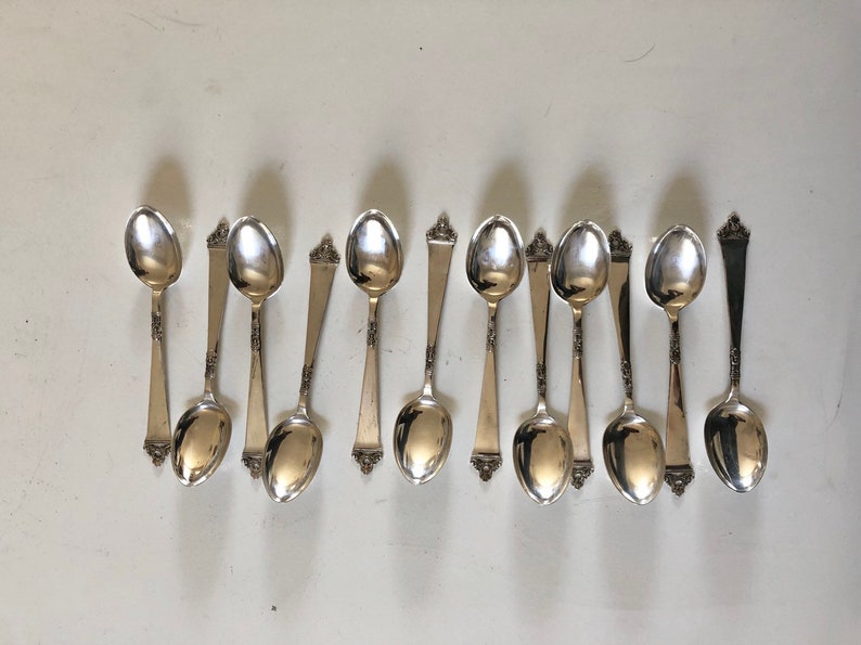 Puede incluir: Un juego de doce cucharaditas de plata con mangos adornados.