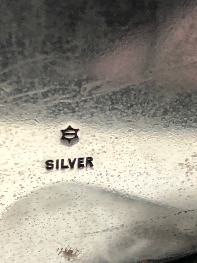 May include: Close-up of a silver object with a star-shaped mark and the word "SILVER" inscribed on it.