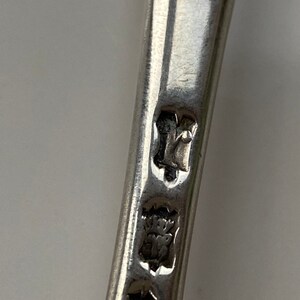 K&ouml;nnte beinhalten: Nahaufnahme der Stempel auf einem silbernen L&ouml;ffel. Die Stempel umfassen eine Krone, einen Buchstaben "Y" und eine Herstellermarke.
