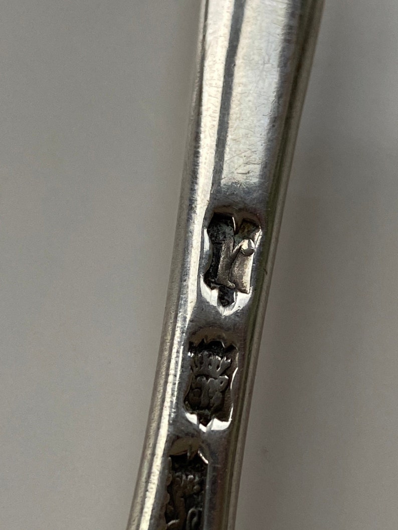 K&ouml;nnte beinhalten: Nahaufnahme der Stempel auf einem silbernen L&ouml;ffel. Die Stempel umfassen eine Krone, einen Buchstaben "Y" und eine Herstellermarke.