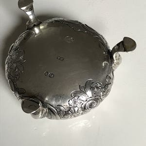 以下が含まれることがあります： 装飾的な花柄が施された銀製の足付きボウル。ボウルは3本の足があり、「W.P.」と「GD」の文字が刻印されています。