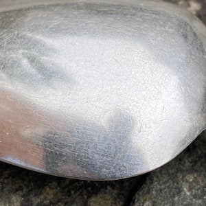 May include: Close-up of a silver spoon with a smooth, shiny surface. The spoon has a rounded bowl and a long, slender handle.