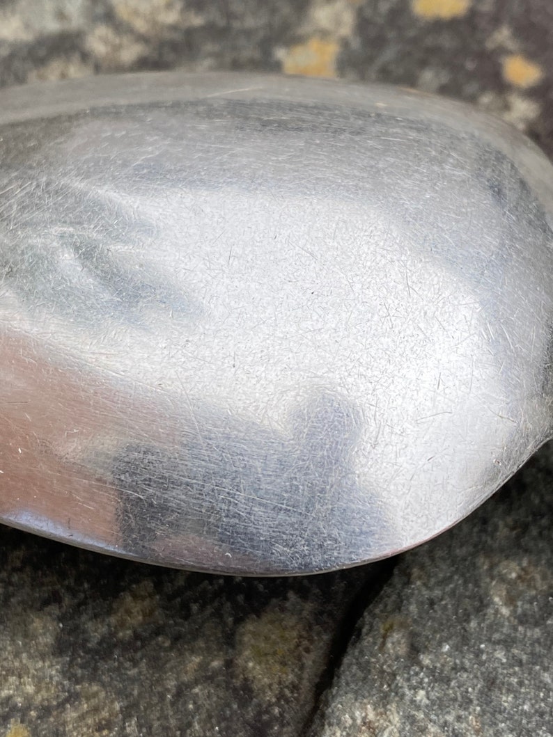 May include: Close-up of a silver spoon with a smooth, shiny surface. The spoon has a rounded bowl and a long, slender handle.