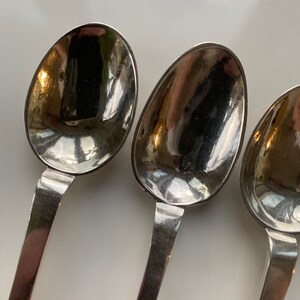 May include: Three silver spoons with rounded bowls and simple handles. The spoons are arranged in a row, with the bowls facing the viewer.