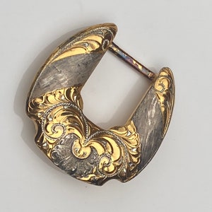 May include: A gold and silver belt buckle with intricate floral designs. The buckle is made of metal and has a polished finish.