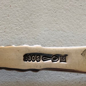 Puede incluir: Primer plano de una cuchara de plata con la inscripci&oacute;n "330S" y una peque&ntilde;a marca cuadrada con la letra "N" en su interior.