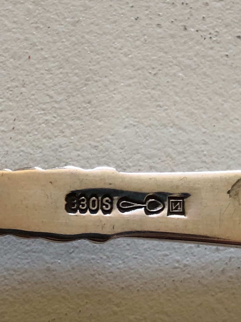 Puede incluir: Primer plano de una cuchara de plata con la inscripci&oacute;n "330S" y una peque&ntilde;a marca cuadrada con la letra "N" en su interior.