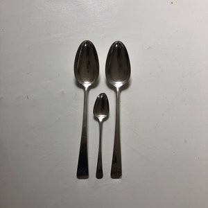 Puede incluir: Tres cucharas de plata de diferentes tama&ntilde;os, dispuestas en fila de la m&aacute;s grande a la m&aacute;s peque&ntilde;a. Las cucharas est&aacute;n pulidas y reflejan la luz.