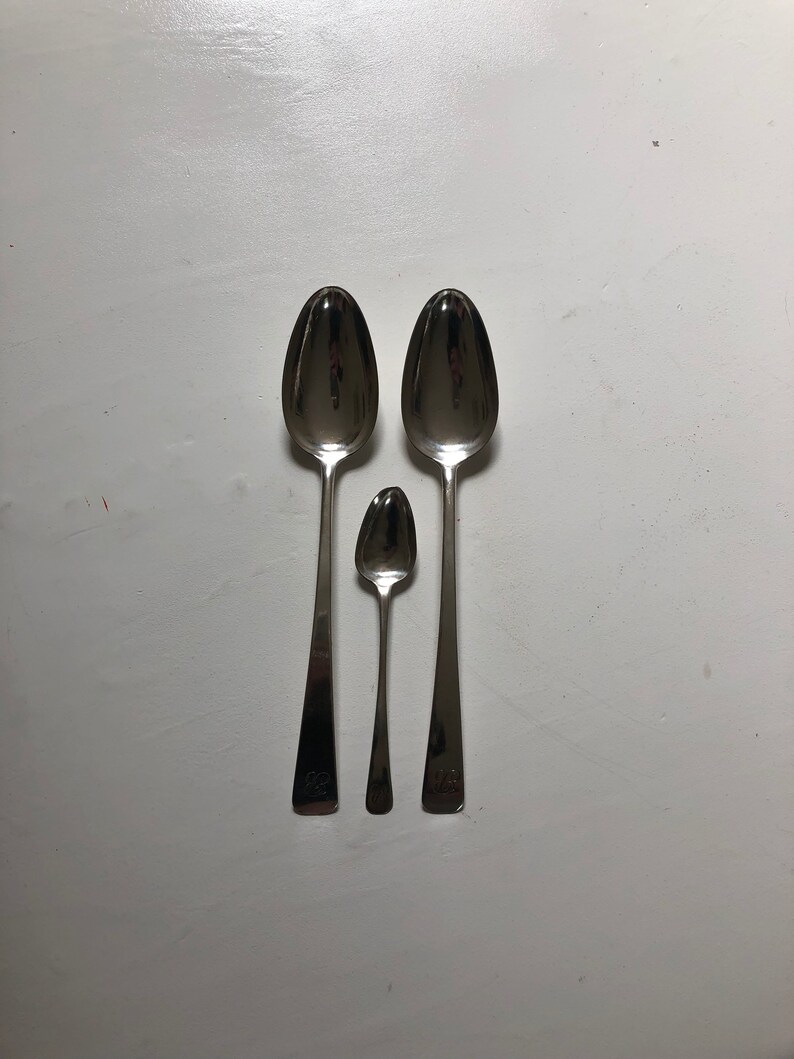 Puede incluir: Tres cucharas de plata de diferentes tama&ntilde;os, dispuestas en fila de la m&aacute;s grande a la m&aacute;s peque&ntilde;a. Las cucharas est&aacute;n pulidas y reflejan la luz.