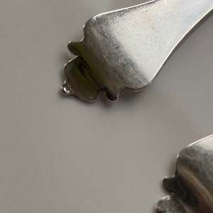 May include: Close-up of the ornate, silver handle of a spoon.
