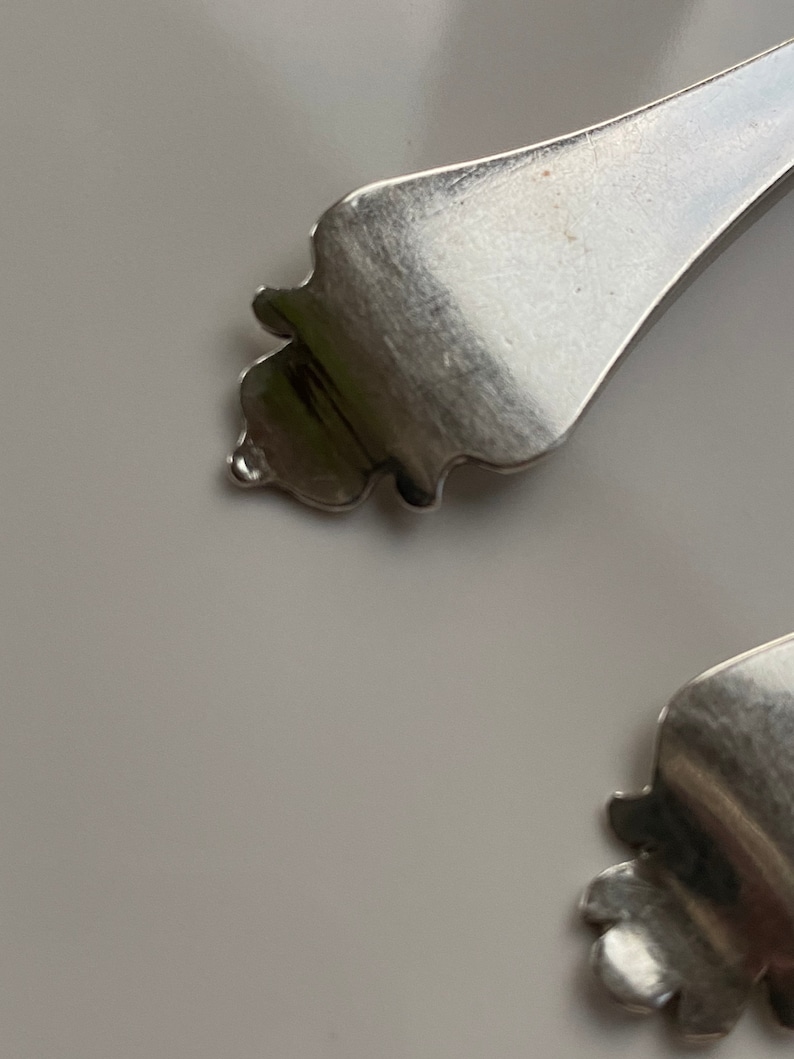 May include: Close-up of the ornate, silver handle of a spoon.