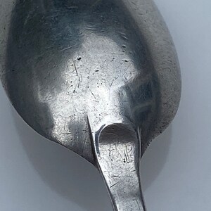 K&ouml;nnte beinhalten: Nahaufnahme der R&uuml;ckseite eines silbernen L&ouml;ffels mit abgenutzter Oberfl&auml;che und Markierungen. Der L&ouml;ffel hat eine abgerundete Schale und einen langen, schlanken Stiel.