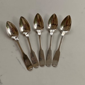 May include: Set of six silver teaspoons with ornate handles. Each spoon has a different name engraved on the handle: "Clara", "Laura", "Emma", "Alice", "Grace", and "Jane".