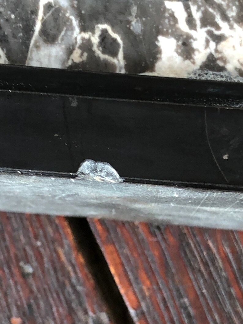 May include: Close-up of a black window frame with a small white paint chip on the bottom edge. The frame is above a dark brown wooden surface.
