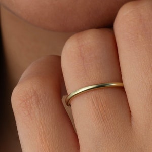 Puede incluir: Un anillo de banda de oro fino y pulido con una superficie lisa y redondeada. El anillo presenta un diseño circular continuo y minimalista que se asienta cómodamente en el dedo, mostrando un acabado en oro amarillo metálico brillante.