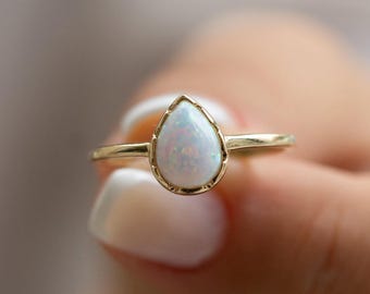 Puede incluir: Un anillo de oro con una piedra de ópalo blanco en forma de lágrima.