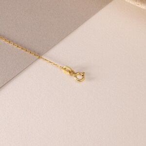 May include: A delicate gold chain necklace featuring a small, circular spring ring clasp and a flat, rectangular connector link. The fine metal links are uniform in size and shape, creating a continuous, slender strand of polished yellow gold.