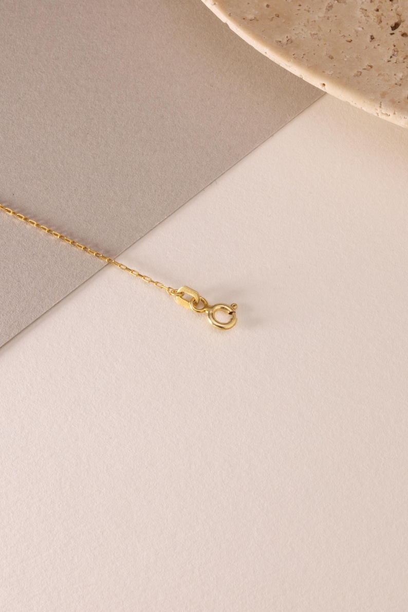 May include: A delicate gold chain necklace featuring a small, circular spring ring clasp and a flat, rectangular connector link. The fine metal links are uniform in size and shape, creating a continuous, slender strand of polished yellow gold.