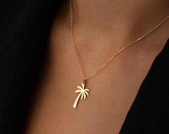 May include: A gold necklace with a palm tree pendant. The necklace is on a model wearing a black shirt.