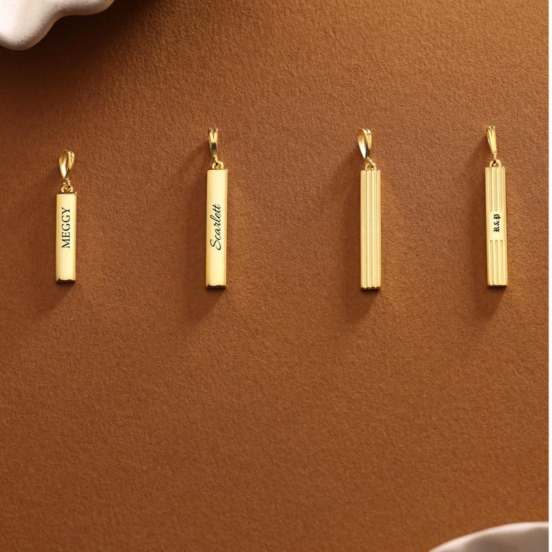 May include: Four gold-colored pendant necklaces. Two pendants have names engraved: "Meggy" and "Scarlett". The other two pendants have a ribbed design and initials "R&P". All pendants have a small loop at the top for a chain.
