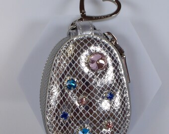 May include: A silver coin purse with a heart-shaped keychain. The purse is decorated with rhinestones in various colors, including blue, pink, and clear.