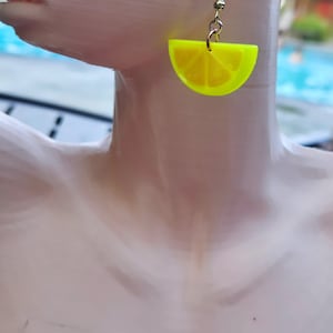 以下が含まれることがあります： 黄色のレモンのスライス形のイヤリングのペア。イヤリングはプラスチック製で、金色のフックが付いています。