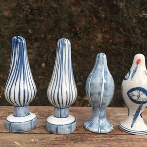 May include: Four ceramic decorative objects in blue and white. Two have vertical striped patterns, one has a watercolour effect, and the last has a unique design with a wheel and red accents. The objects are on a wooden surface.
