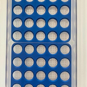 May include: A clear plastic storage container with a blue silicone insert. The insert has 50 round compartments.