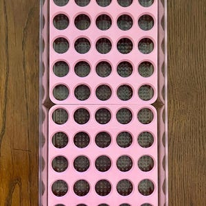 May include: A clear plastic storage container with a pink silicone insert. The insert has 48 round compartments.