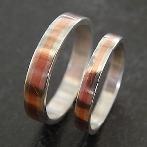May include: Two silver wedding bands with a thin copper inlay. The bands are stacked on top of each other.