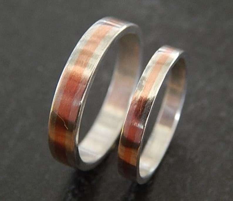 May include: Two silver wedding bands with a thin copper inlay. The bands are stacked on top of each other.