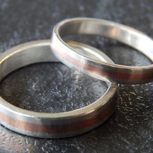 May include: Two silver wedding bands with a thin copper band around the edge of each ring.