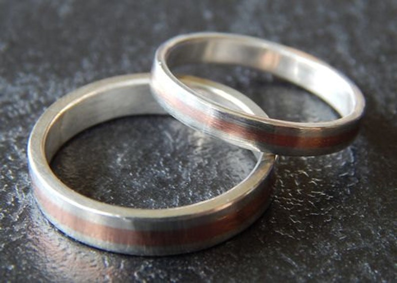 May include: Two silver wedding bands with a thin copper band around the edge of each ring.
