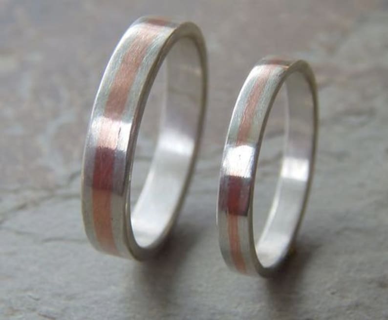 May include: Two silver wedding bands with a thin copper inlay. The bands are stacked on top of each other.