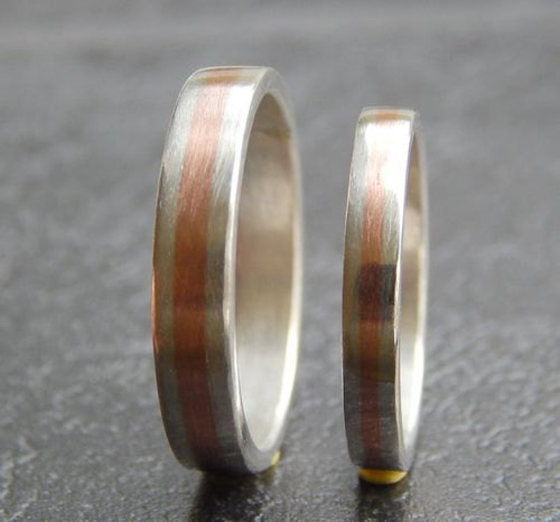 May include: Two silver wedding bands with a thin copper stripe down the center.