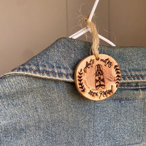 Puede incluir: Una etiqueta de madera con el texto "Anti mites 100% Natural" y un dibujo de una polilla. La etiqueta está unida a una chaqueta vaquera con una cuerda.