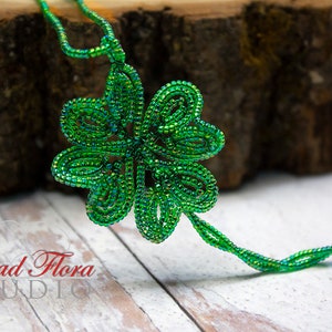 May include: A green beaded four-leaf clover pendant with a long beaded chain. The pendant is made of small, iridescent green beads and is shaped like a four-leaf clover. The chain is also made of small, iridescent green beads and is long enough to be worn as a necklace.