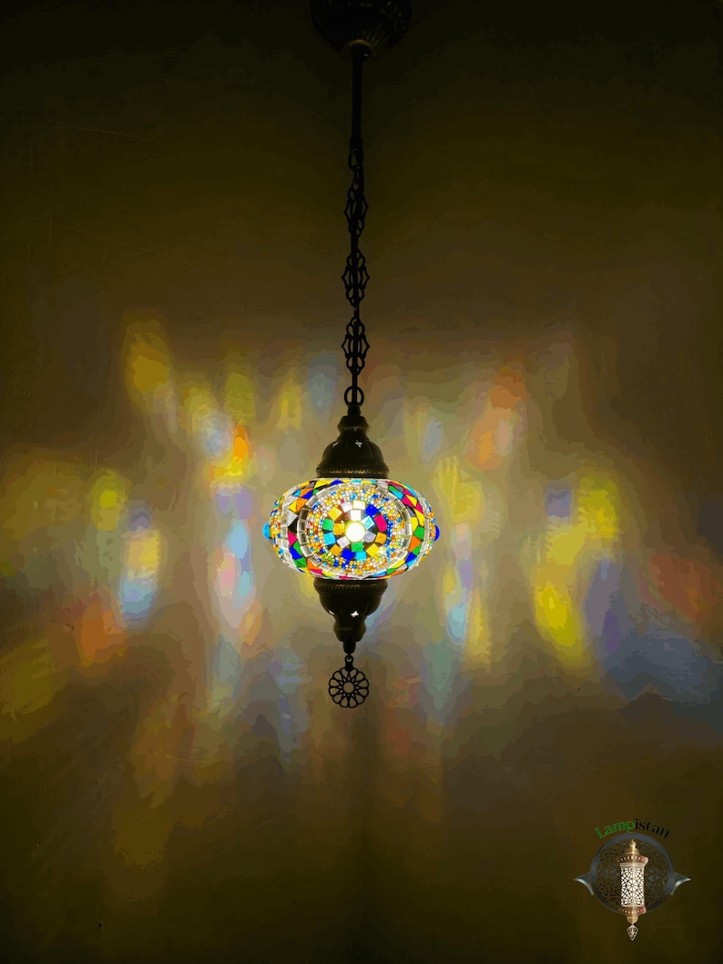 Op de afbeelding: Een kleurrijke moza&iuml;ek glazen hanglamp met een ronde, bolvormige kap. De lamp hangt aan een ketting en heeft een metalen voet.
