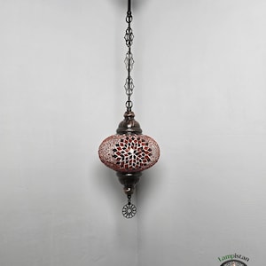 Op de afbeelding: Een hangende moza&iuml;ekglazen lamp met een rood en wit geometrisch patroon. De lamp heeft een zwarte metalen ketting en een decoratief metalen eindstuk.